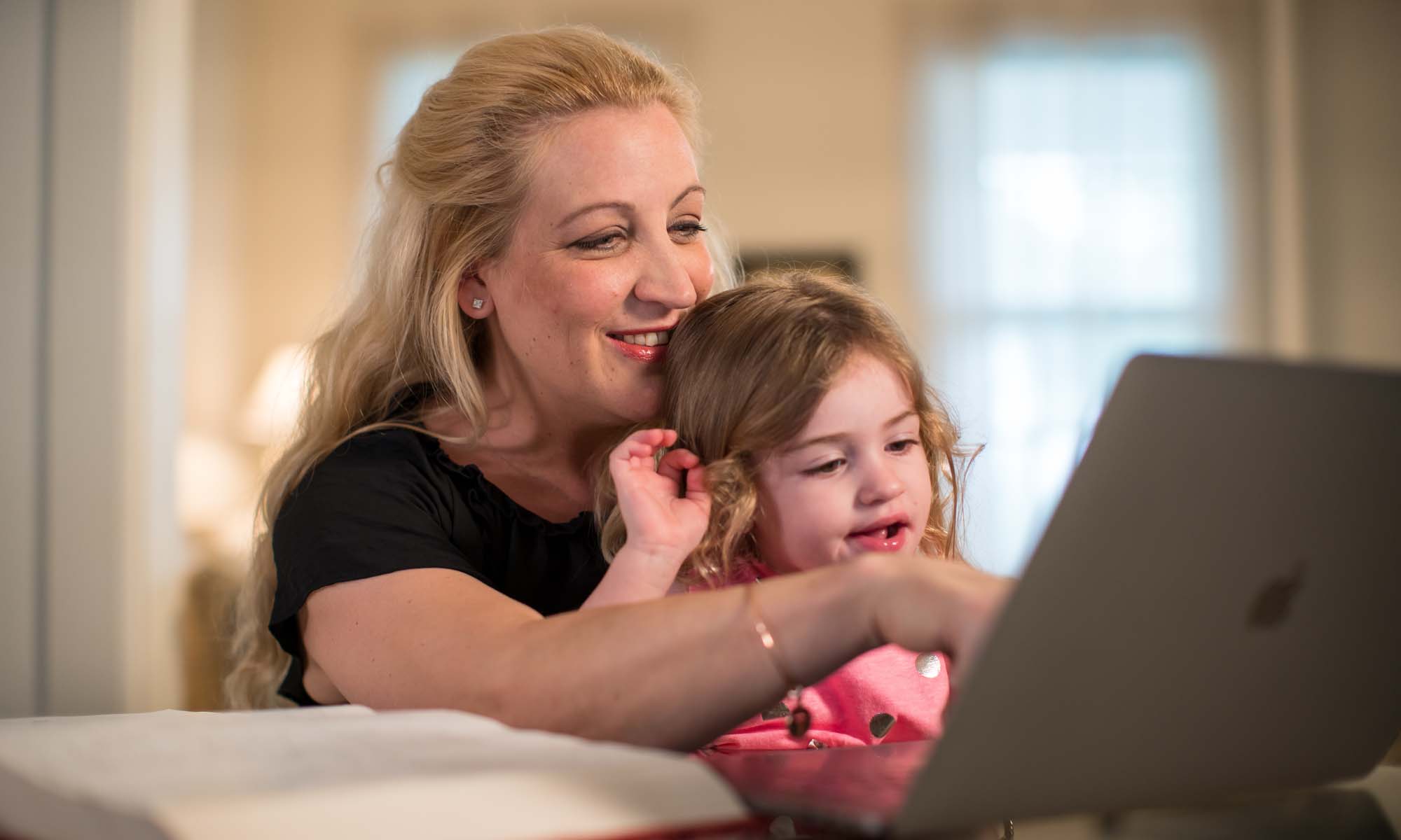 Mother working on laptop with daughter on her lap