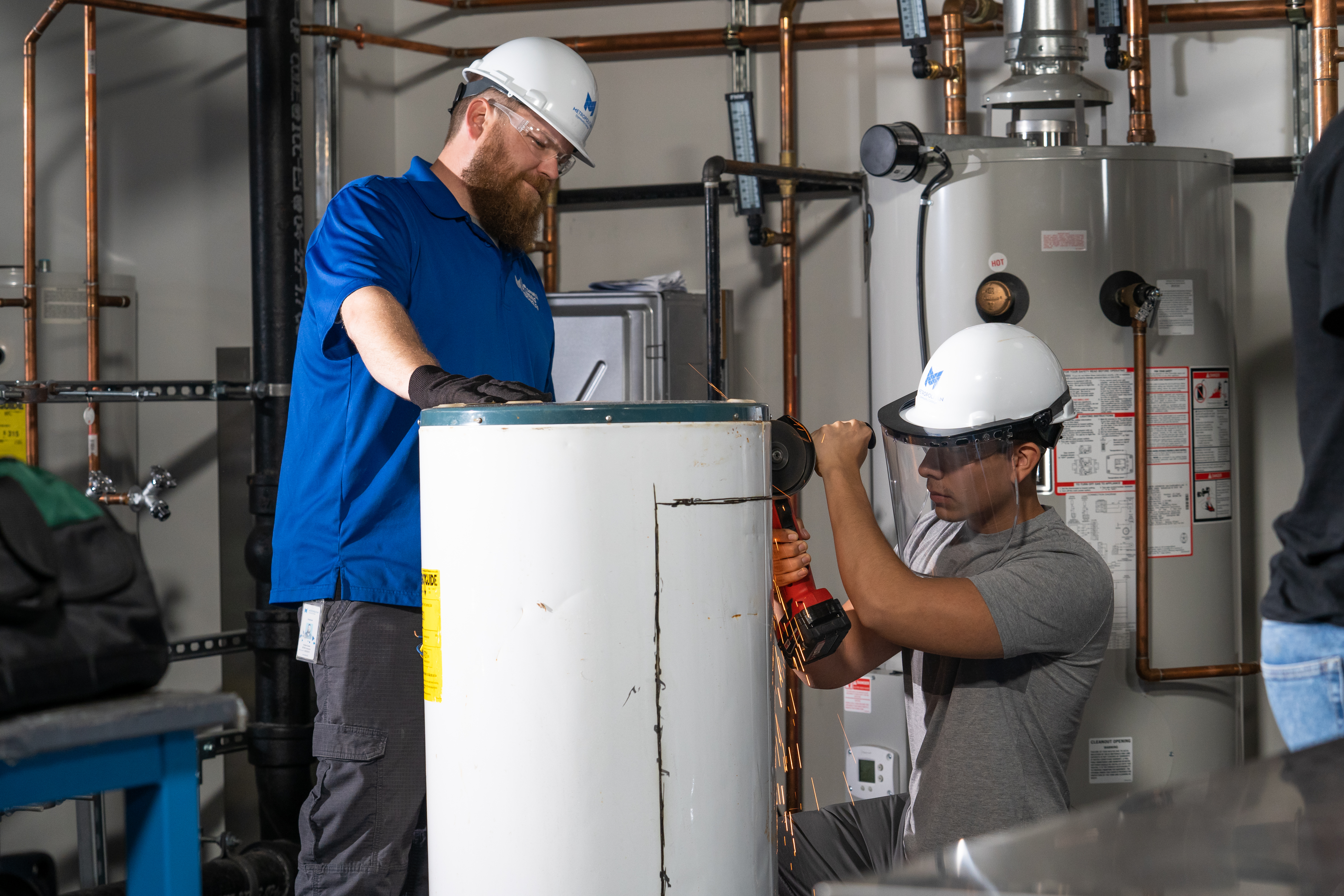 Two men working on a hot water tank in a classroom setting. 