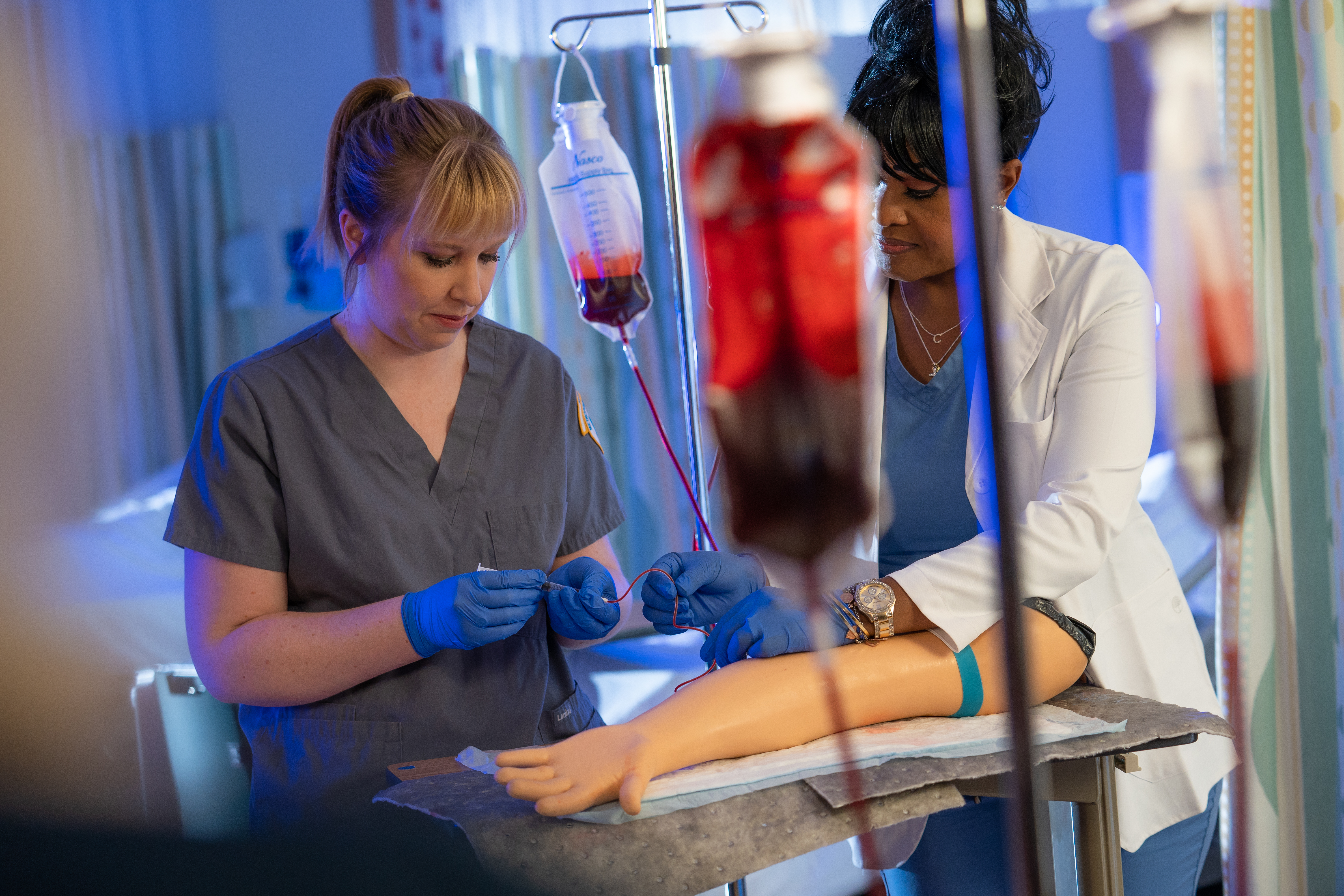 Woman in blue medical scrubs drawing blood from female patient in a white sweater. 