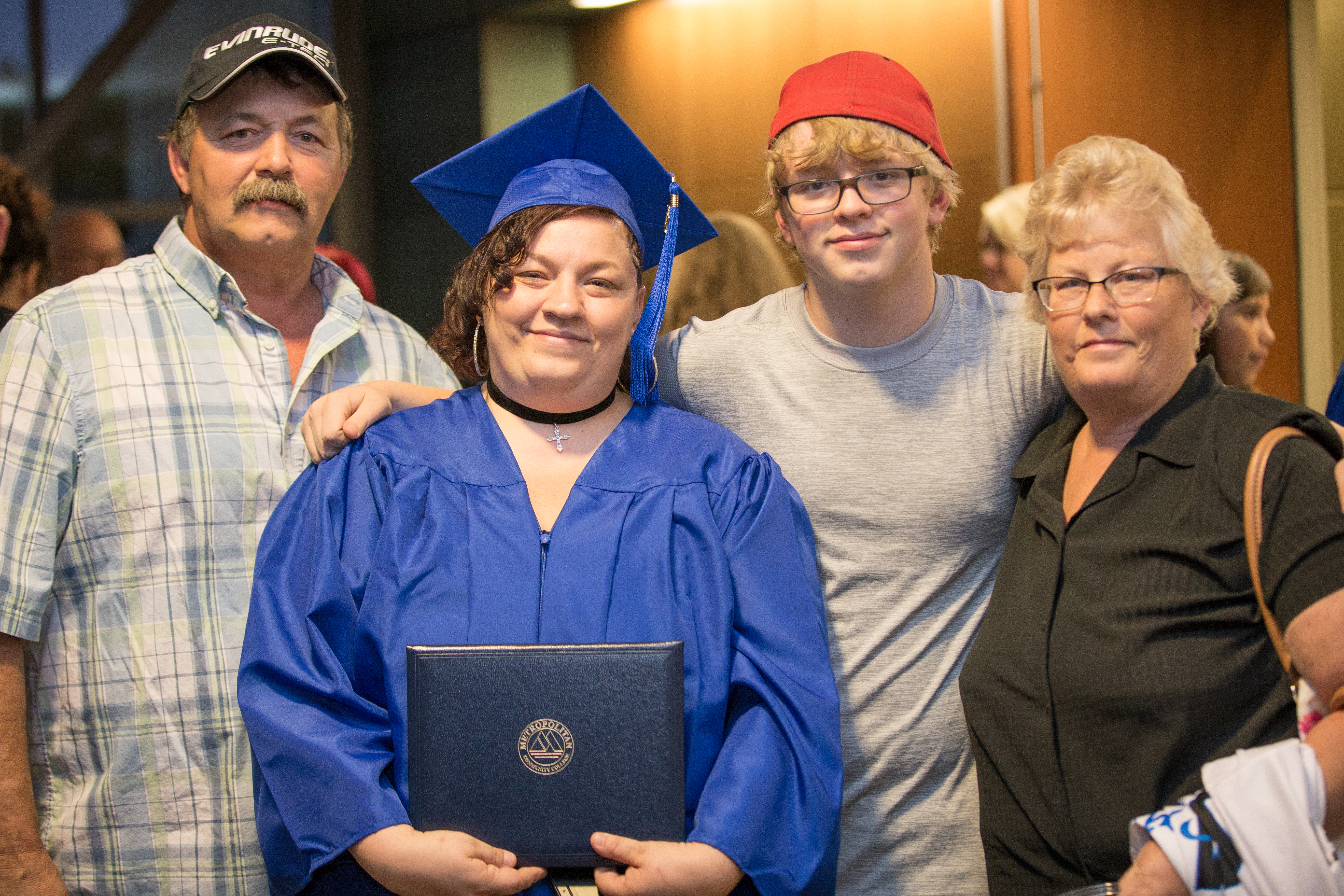 GED graduate in blue gown standing with two men and a woman. 