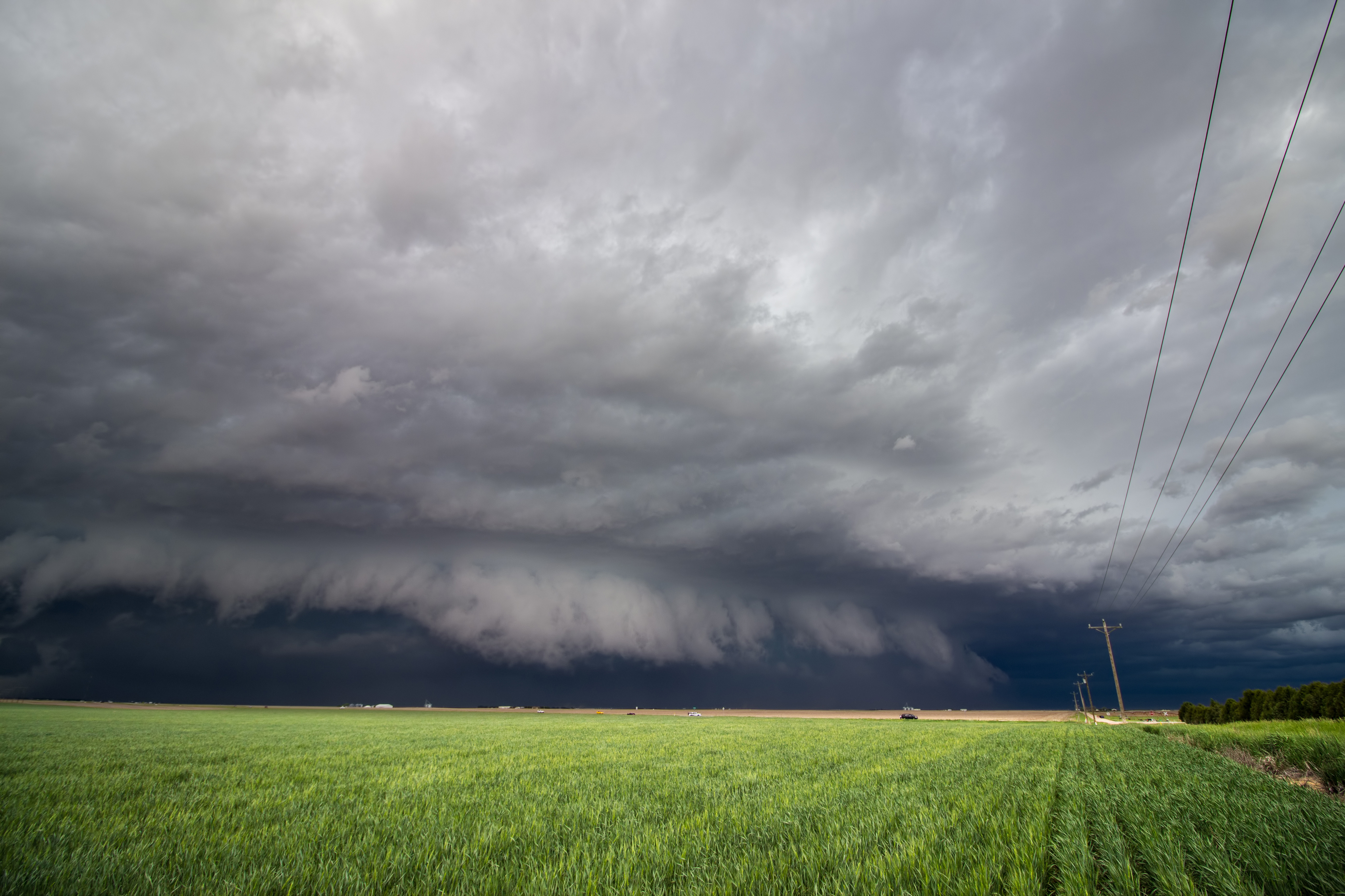 ominous gray clouds move in over a rural field with power lines bordering the right side